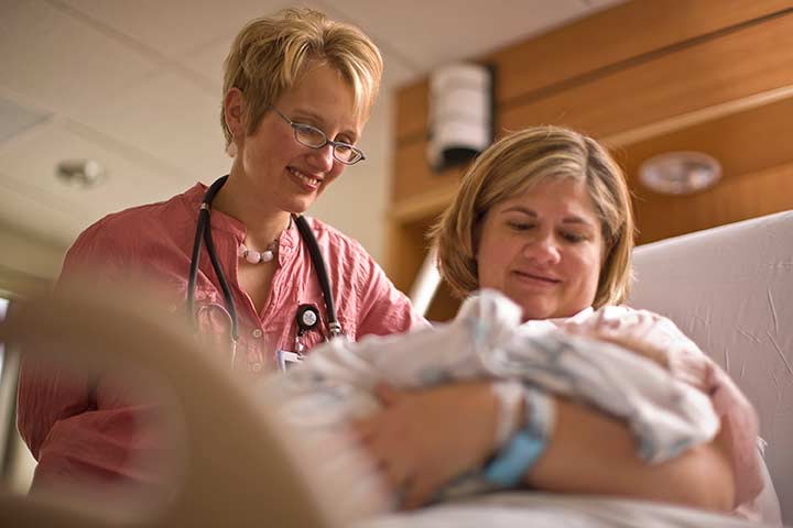 New-mom-holding-baby-female-nurse-smile1.jpg